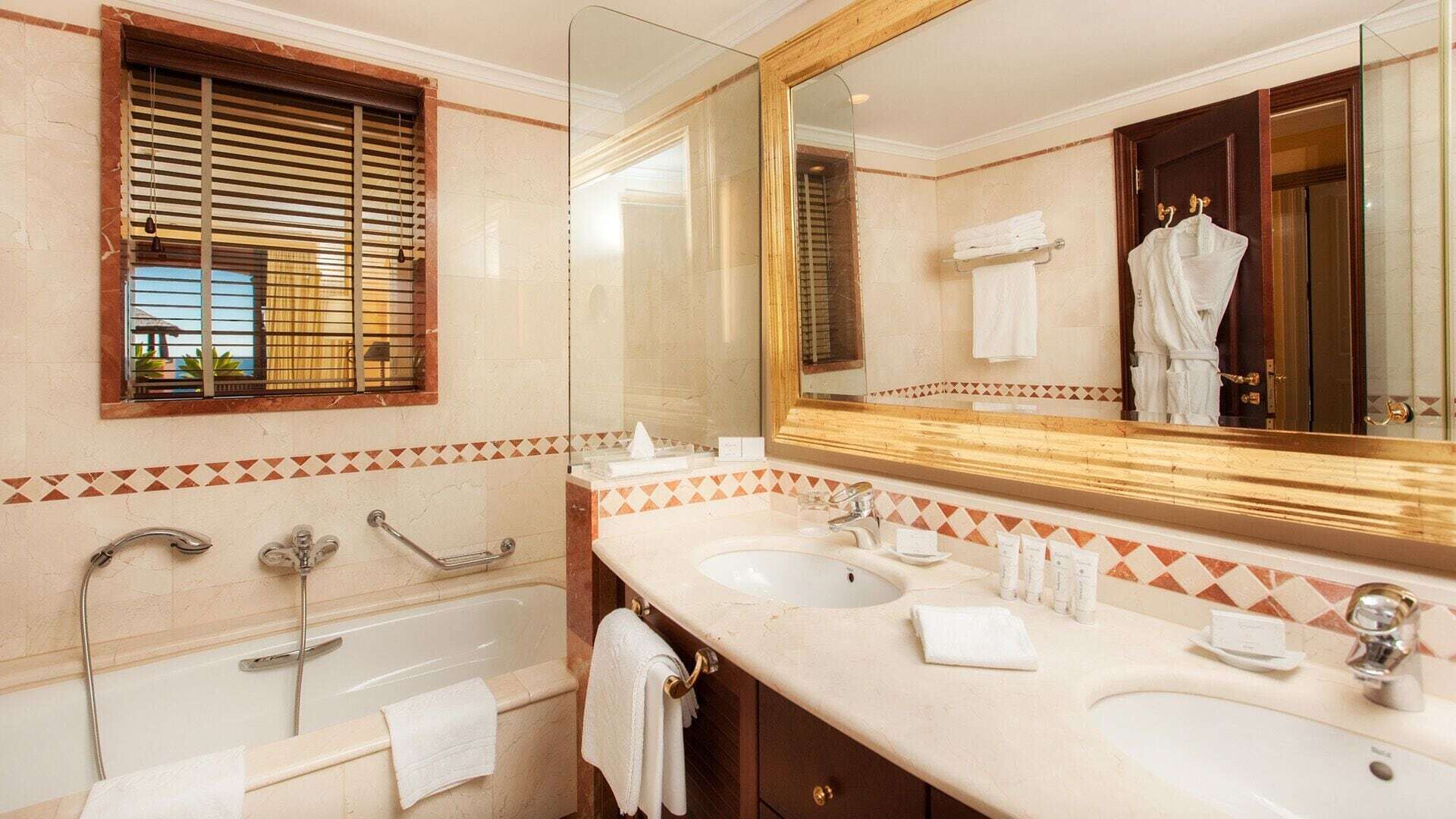 Un baño con bañera, dos lavamanos, un espejo grande y una ventana con persianas.