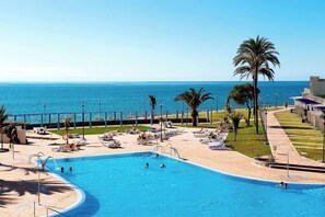 A pool area with a view of the sea, palm trees, and lounge chairs. - Grupotel Playa Feliz (San Bartolomé de Tirajana)