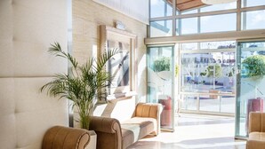 A modern lobby with leather sofas, a large potted plant, and a glass entrance leading outside. - Grupotel Playa Feliz (San Bartolomé de Tirajana)