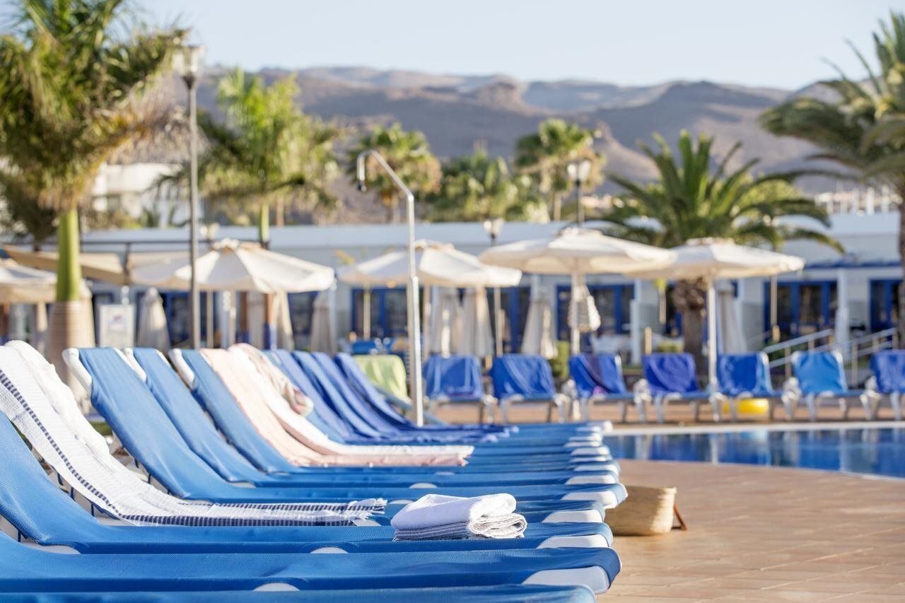 Une rangée de chaises longues avec des serviettes, des parasols et une piscine en arrière-plan.