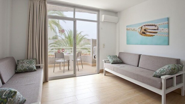 A modern living room with a sofa, a dining table with chairs, and a sliding glass door leading to a balcony. - Club Sa Coma (Sant Llorenc des Cardassar)