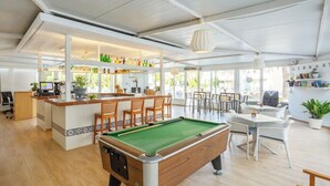 A pool table in a bright room with a bar area and seating. - Club Sa Coma (Sant Llorenc des Cardassar)