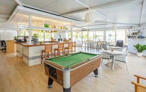 A pool table in a bright room with a bar area and seating. - Club Sa Coma (Sant Llorenc des Cardassar)