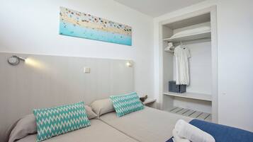 Un dormitorio con cama, dos almohadas, una obra de arte en la pared, un armario con ropa colgada y una toalla sobre la cama.