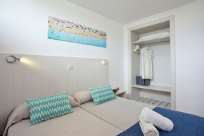 Un dormitorio con cama, dos almohadas, una obra de arte en la pared, un armario con ropa colgada y una toalla sobre la cama.