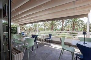 An outdoor seating area with tables and chairs, a covered section, and a view of palm trees. - Travelodge Alicante Puerto (Alicante)