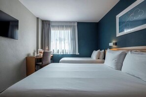 A hotel room with two beds, a desk, a chair, a TV, and a window with curtains. - Travelodge Alicante Puerto (Alicante)