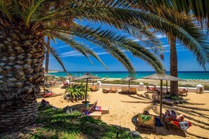 Ein Strand mit Palmen, Liegestühlen und Sonnenschirmen.