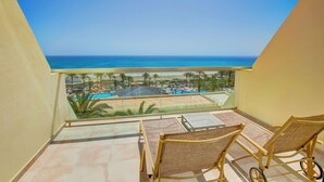 A balcony with two wicker chairs, a tiled floor, and a view of a pool and beach. - Sbh Costa Calma Palace (Pajara)