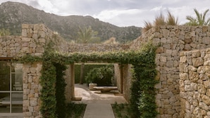 A stone-walled pathway leading to a covered area with a bench, surrounded by greenery and a mountainous backdrop. - Es Raco D Arta, a Member of Design Hotels (Arta)