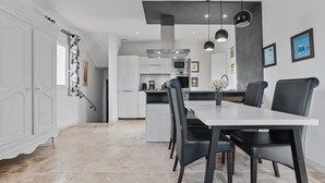 Une cuisine moderne avec des meubles blancs, un coin repas doté d’une table blanche et de chaises noires, et un luminaire suspendu.