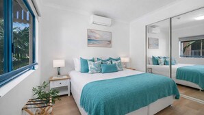 Een slaapkamer met een groot bed, nachtkastje, spiegel en raam.