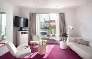 A modern hotel room with a flat-screen TV, a sofa, a chair, a coffee table, and a large window with curtains. - Allegro Barcelona (Barcelona)