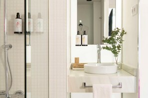 A bathroom with a glass shower enclosure, a white sink with a mirror above it, and toiletries on the sink counter. - Allegro Barcelona (Barcelona)
