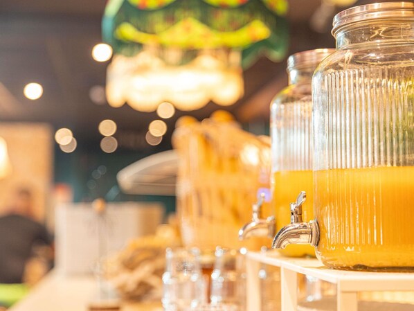 En dryckesdispenser med en genomskinlig glasbehållare fylld med orangefärgad vätska, en kran och en suddig bakgrund med ljus.