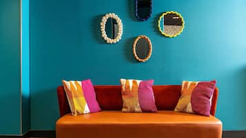Pared verde azulada con cuatro espejos decorativos y un sofá rojo con cojines coloridos.
