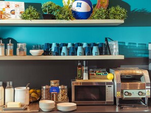 A breakfast bar with coffee mugs, a microwave, and a coffee machine. - Ibis Budget Valencia Aeropuerto (Manises)