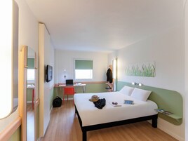 Una habitación de hotel con una cama, un escritorio, una silla, un televisor y una ventana.