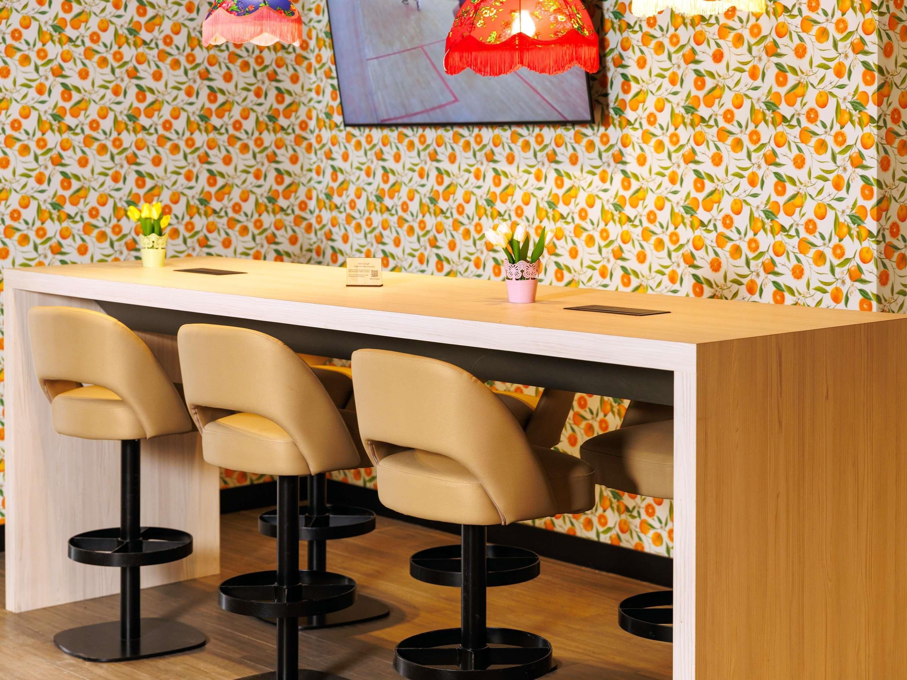 Een bar met een houten toonbank, drie barstoelen, een tafeltje met een QR-code en een muur met een fruitmotief.