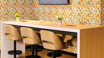Een bar met een houten toonbank, drie barstoelen, een tafeltje met een QR-code en een muur met een fruitmotief.