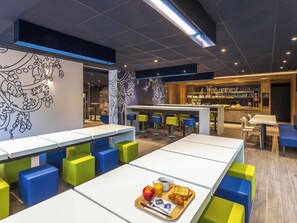 Un área de comedor moderna con mesas altas, taburetes de bar coloridos y una barra.