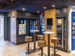 Un interior moderno con máquinas expendedoras, una cafetera y taburetes de bar.