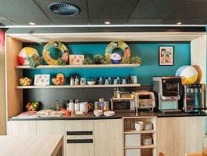 A kitchen area with a coffee machine, microwave, and various food items on the counter. - Ibis Budget Valencia Aeropuerto (Manises)