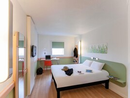 Una habitación de hotel con cama, escritorio, silla, televisor y ventana.