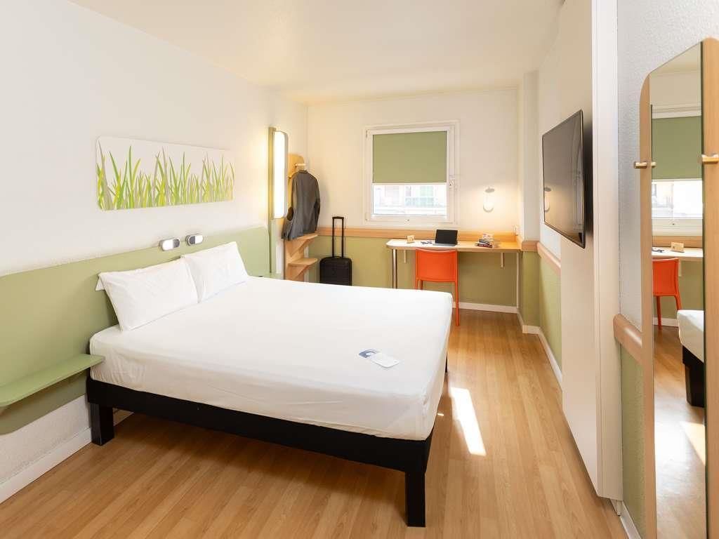 Een hotelkamer met een bed, bureau, stoel, televisie en raam.