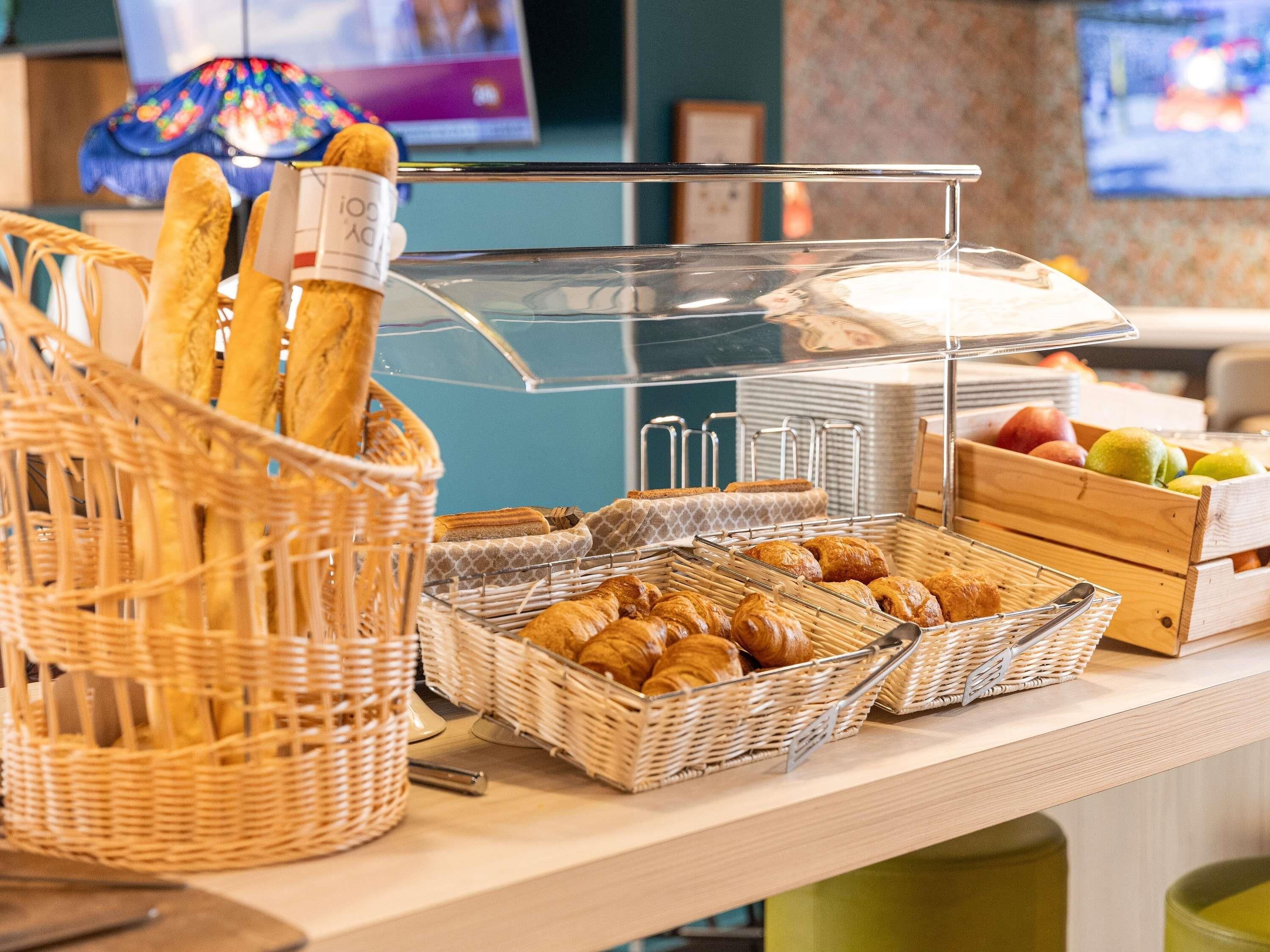 Un bufé con cestas de pan y pasteles, una presentación de frutas y un televisor al fondo.