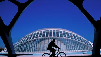 Silueta de una persona en bicicleta frente a un edificio moderno de vidrio con estructura en forma de cúpula.