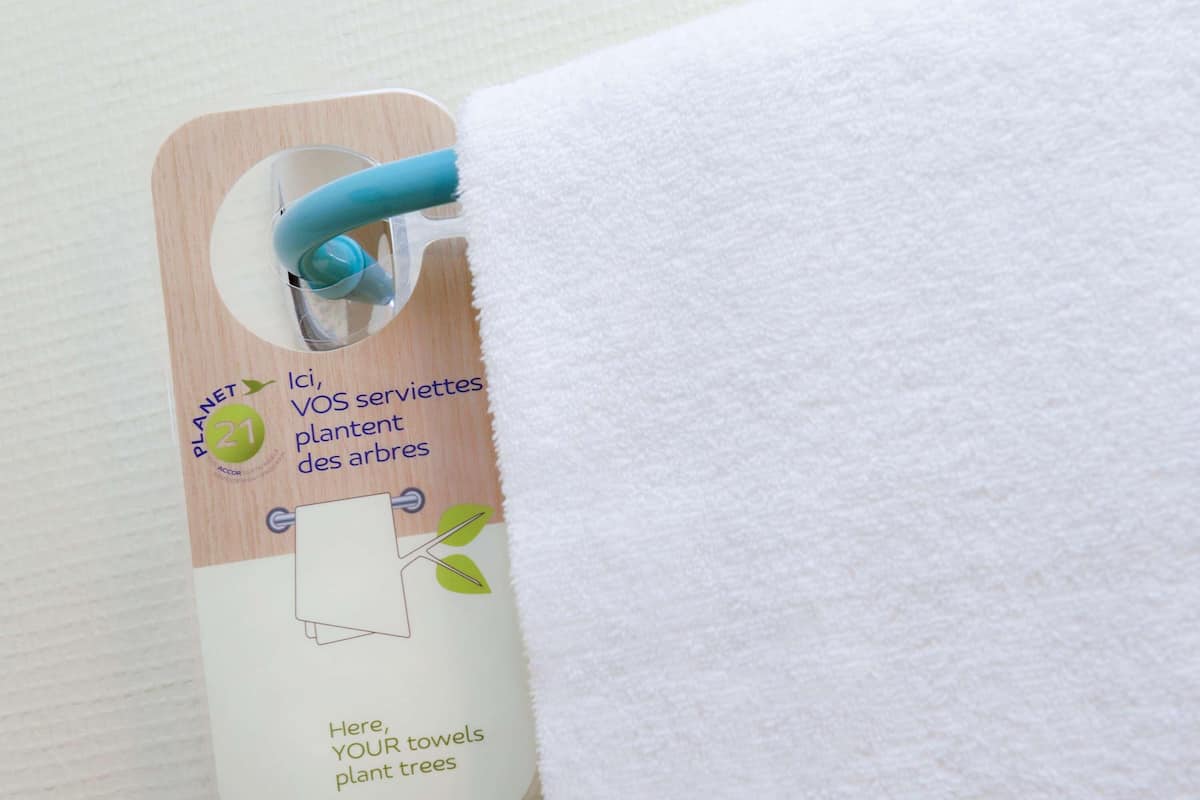A tag attached to a towel with a message about towel reuse for tree planting.