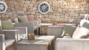 Un muro de piedra con un área de asientos rústica de madera, que incluye una pequeña mesa con un objeto decorativo y un cojín.