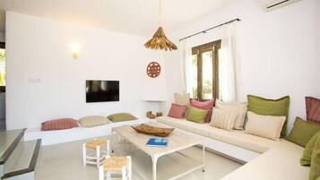 Una sala de estar moderna con un sofá, dos sillones blancos, una mesa de centro y un televisor montado en la pared.
