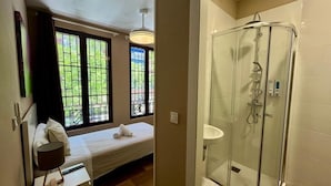 A bedroom with a bed, bedside table, and a window with a view of greenery. - El Palacete de Almudayna (Madrid)