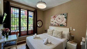 A hotel room with a bed, a desk, a chair, a large window, and a painting. - El Palacete de Almudayna (Madrid)