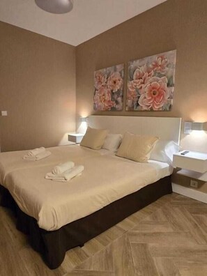 A modern hotel room with a large bed, beige bedding, two wall-mounted paintings of flowers, and bedside lamps. - El Palacete de Almudayna (Madrid)