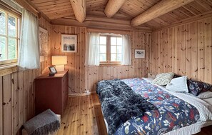 A wooden cabin bedroom with a bed, a nightstand, a lamp, and a window with curtains. - Awesome home in Ljørdalen with sauna (Ljørdalen)