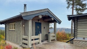 En rustik hytte med træfacade, hoveddør, veranda og skorsten.