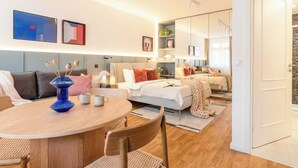 Ein modernes Wohnzimmer mit einem runden Holztisch, einer Couch, einem Bett und einem großen Spiegel.