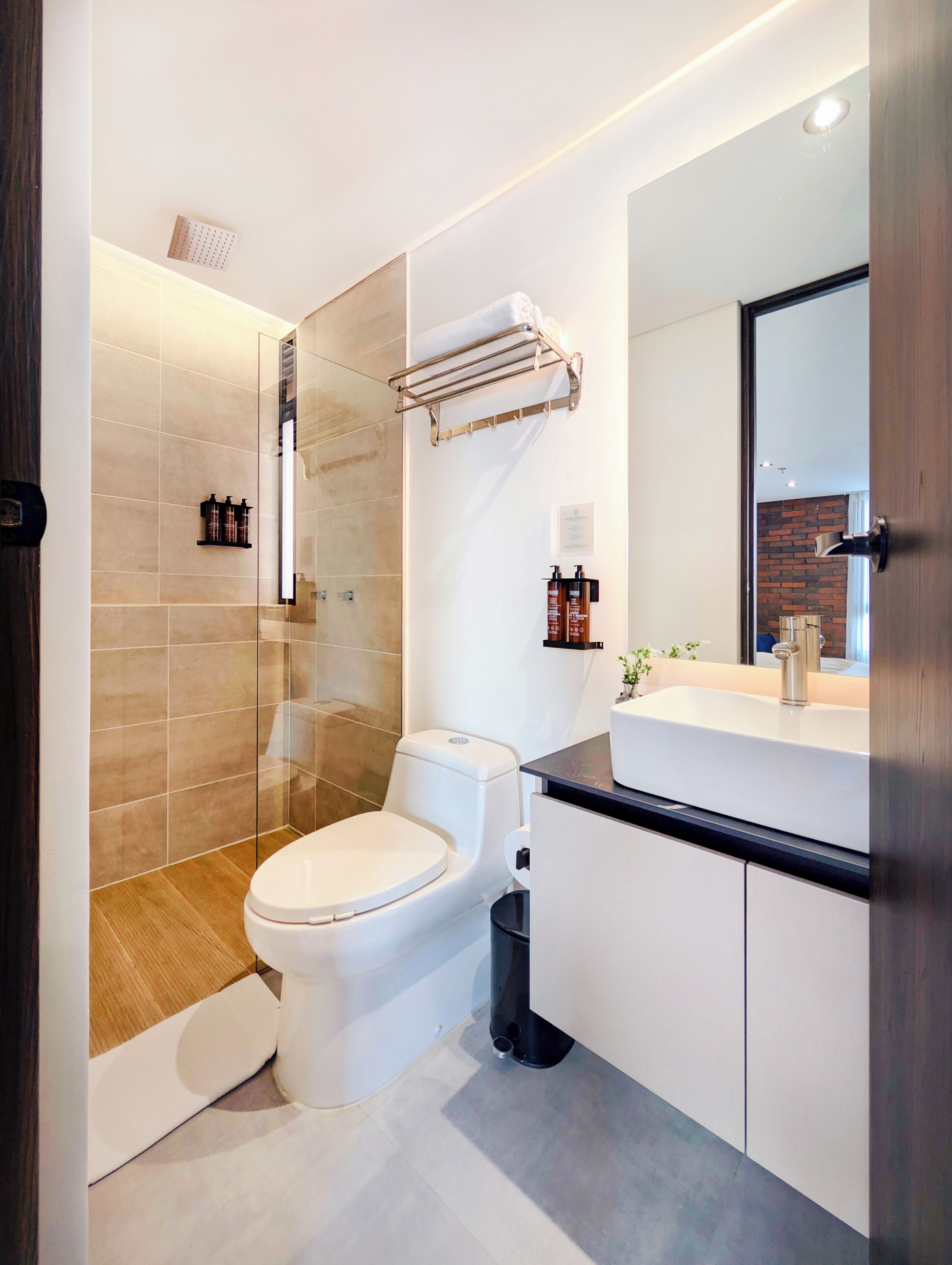A modern bathroom with a glass shower enclosure, a white toilet, a sink with a mirror, and a towel rack.