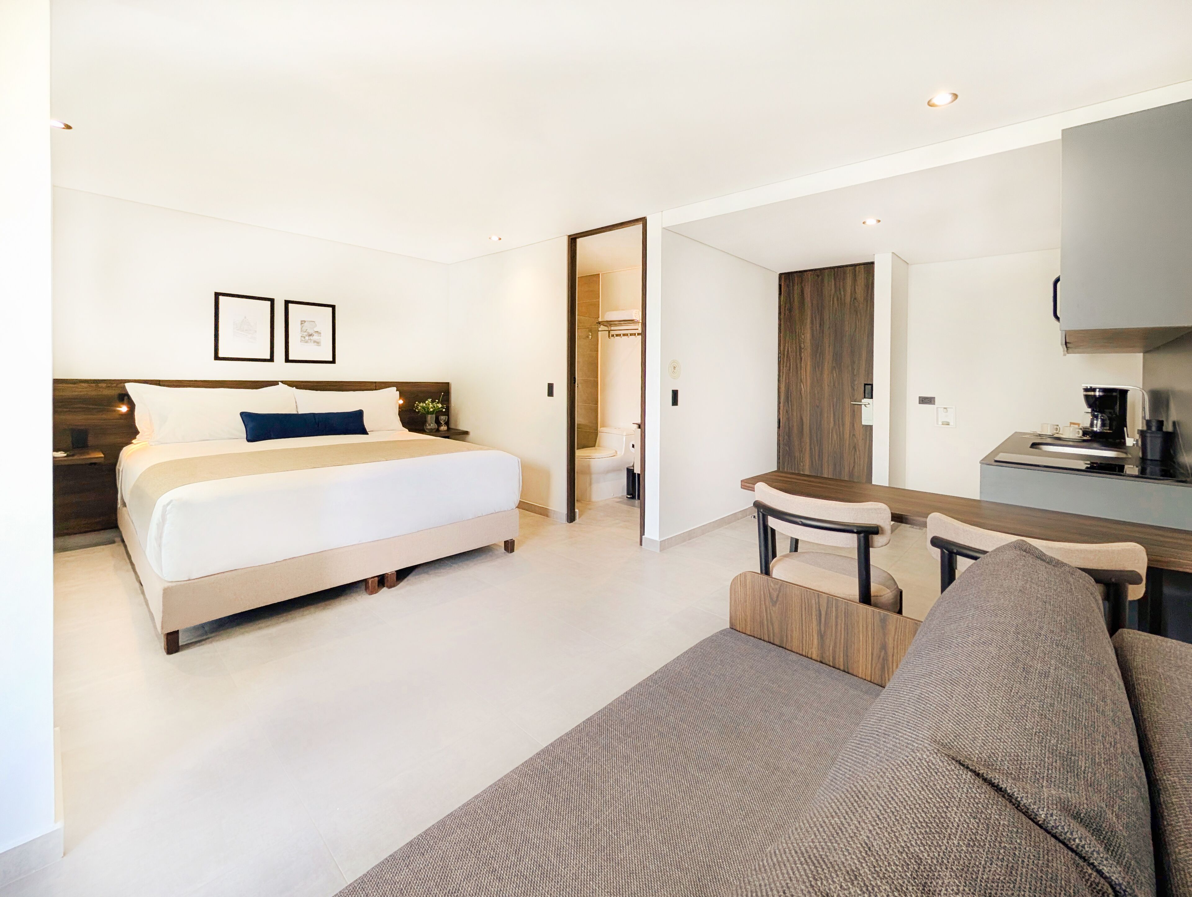 Une chambre d’hôtel moderne dotée d’un grand lit, d’un coin salon avec un canapé et une petite table, ainsi que d’une kitchenette.
