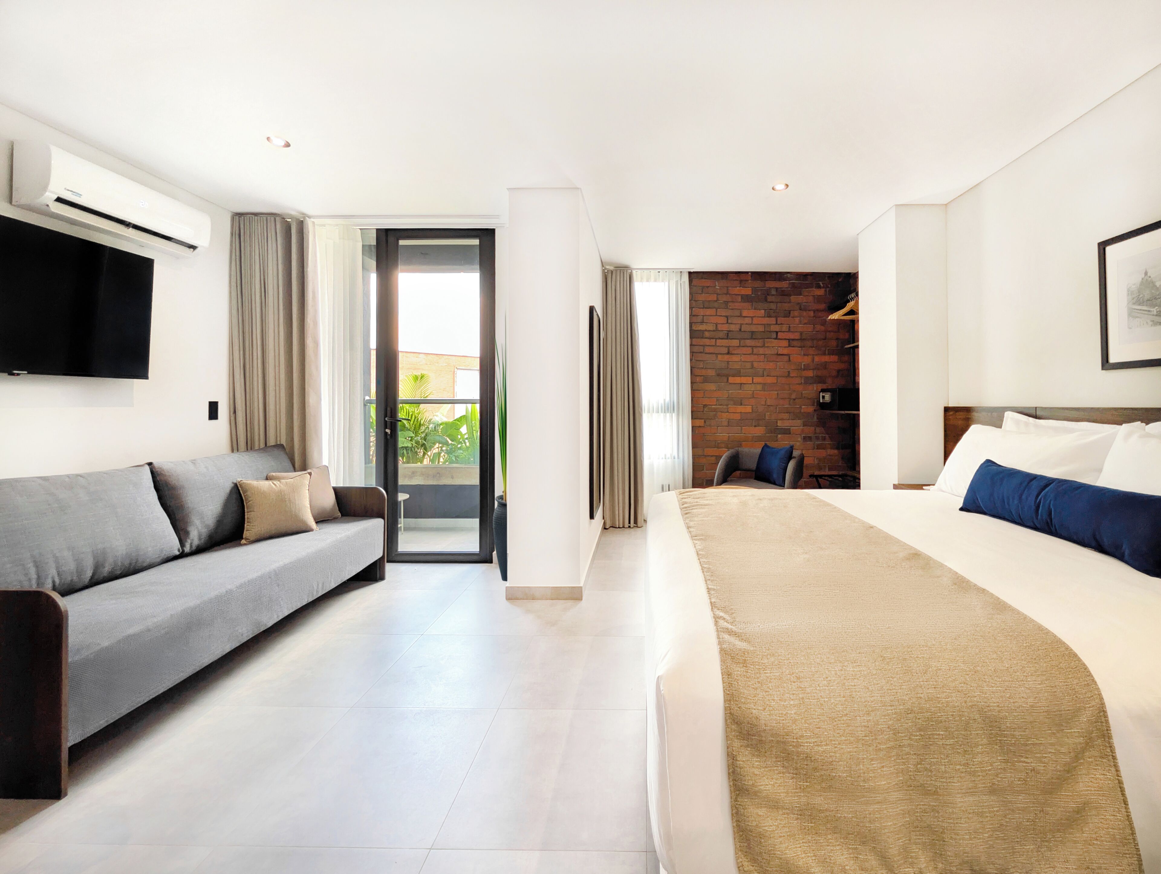 Ein Hotelzimmer mit einer Couch, einem Bett, einem Fernseher und Blick ins Freie.