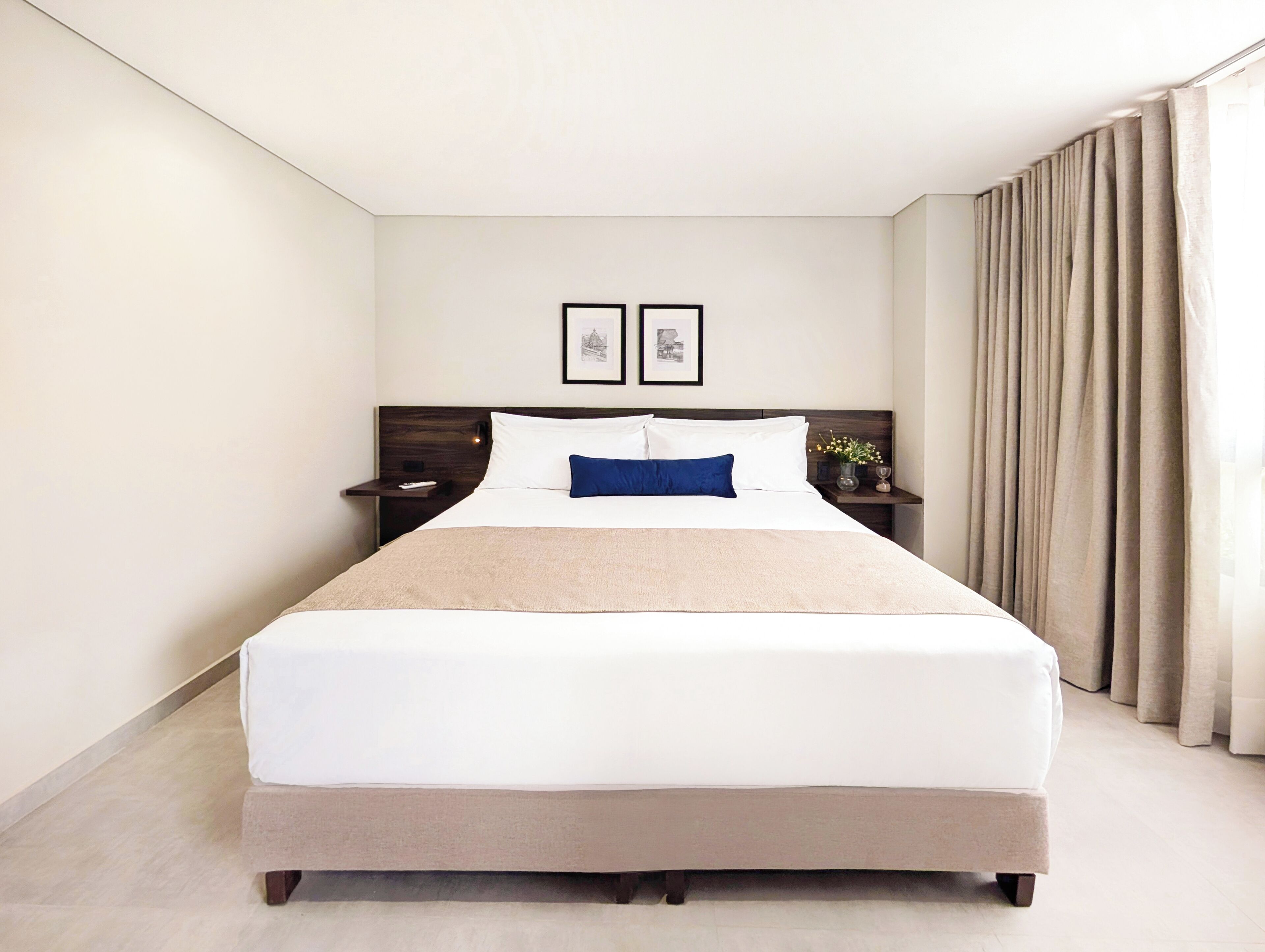 Een hotelkamer met een groot bed, een nachtkastje, een ingelijste foto en een raam met gordijnen.