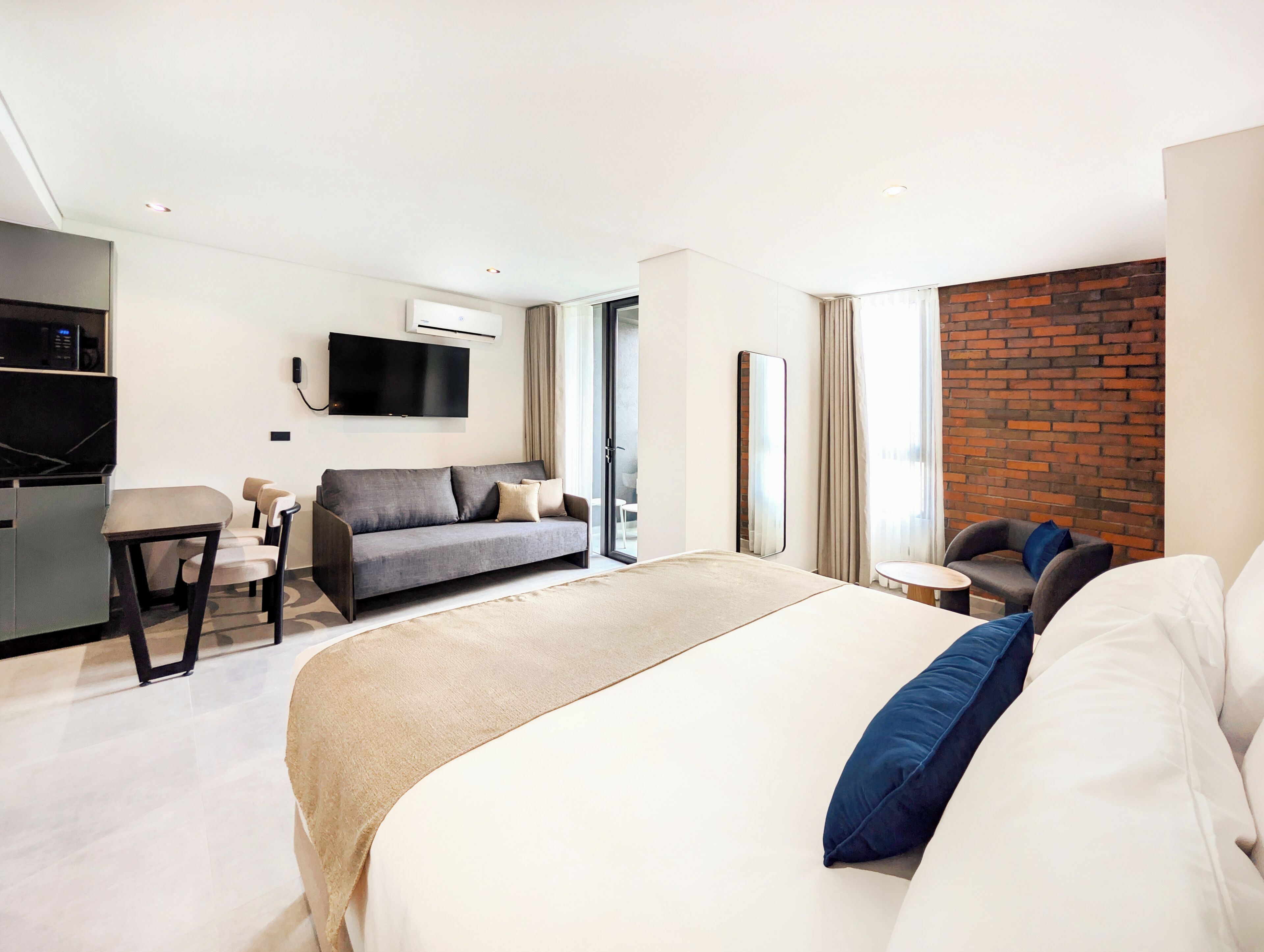 A modern hotel room with a large bed, a sofa, a desk, and a TV.