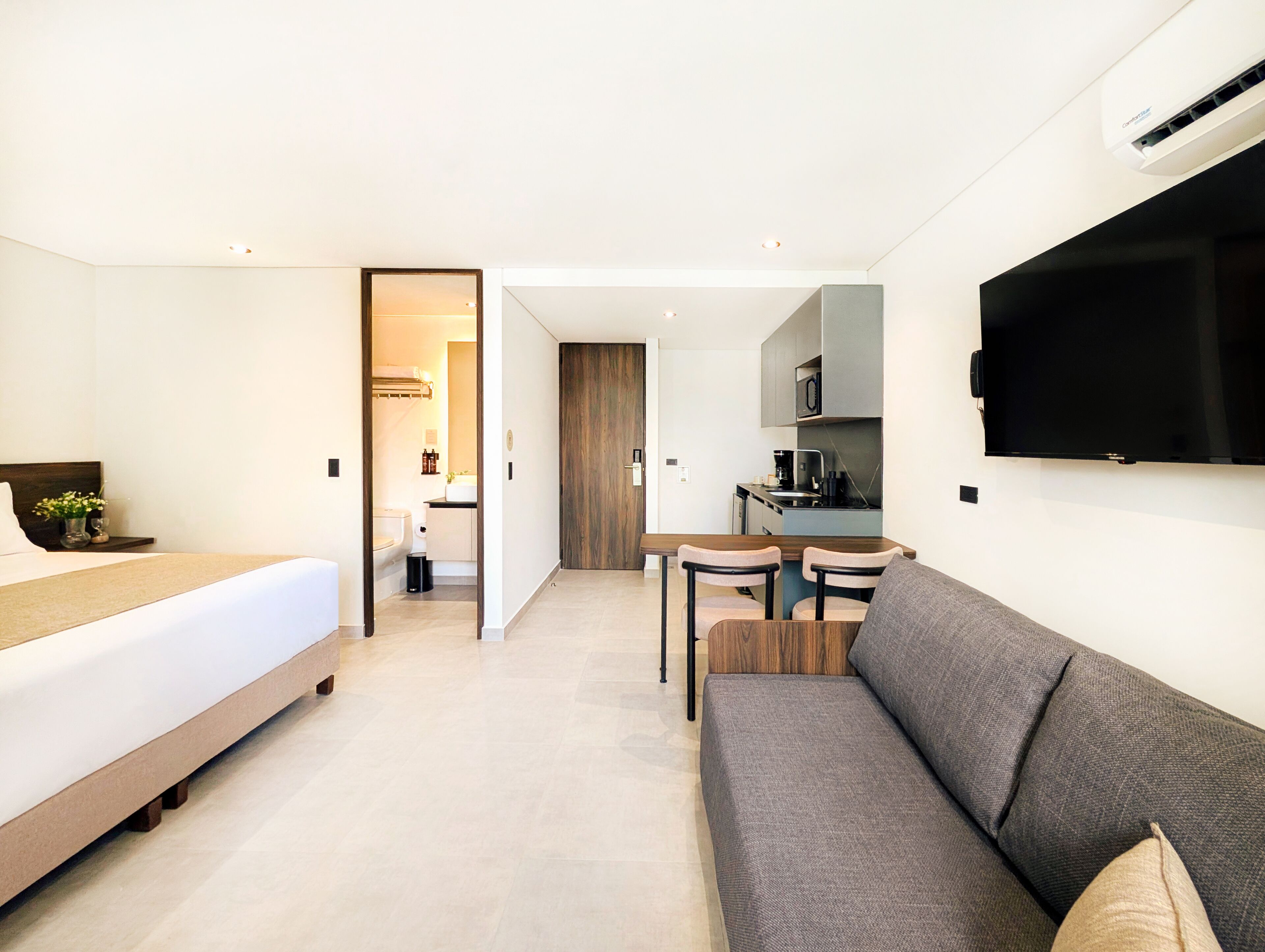 Una habitación de hotel moderna con cama, sofá, televisión, kitchenette y baño.