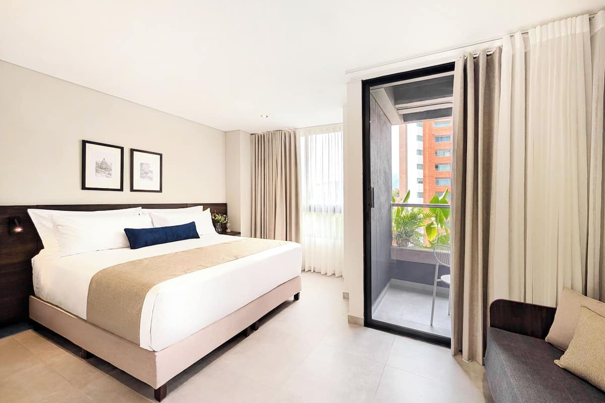 Ein Hotelzimmer mit Bett, einer Couch, einem Balkon mit Vorhängen und gerahmten Bildern an der Wand.