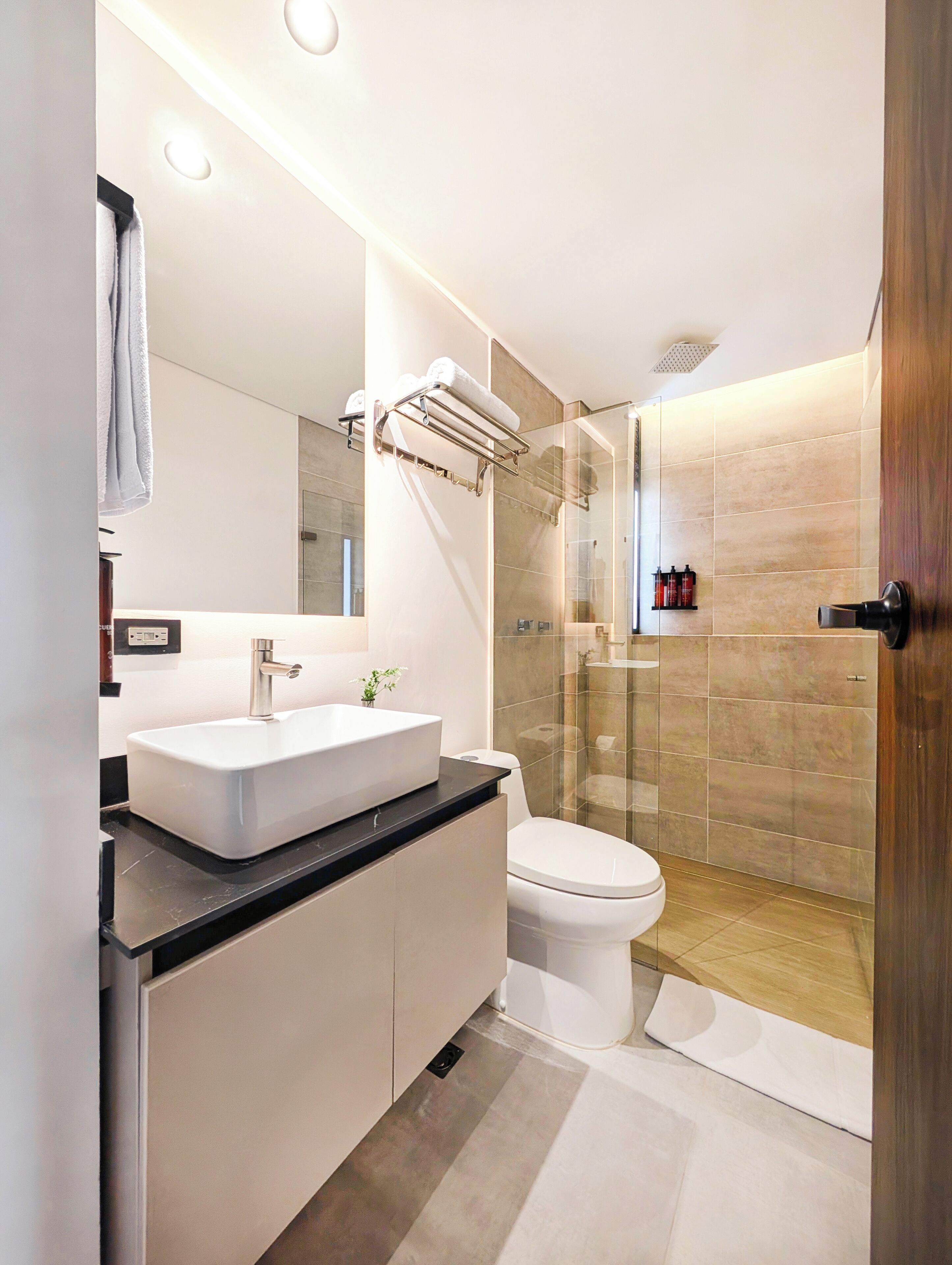 A modern bathroom with a large mirror, a white sink, a toilet, and a glass-enclosed shower.
