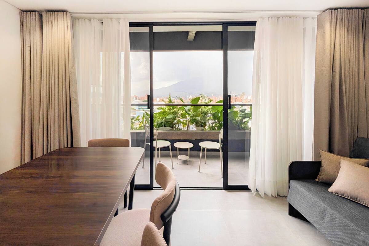 Ein modernes Hotelzimmer mit Esstisch, einer Couch und einem Balkon mit Blick auf die Stadt.