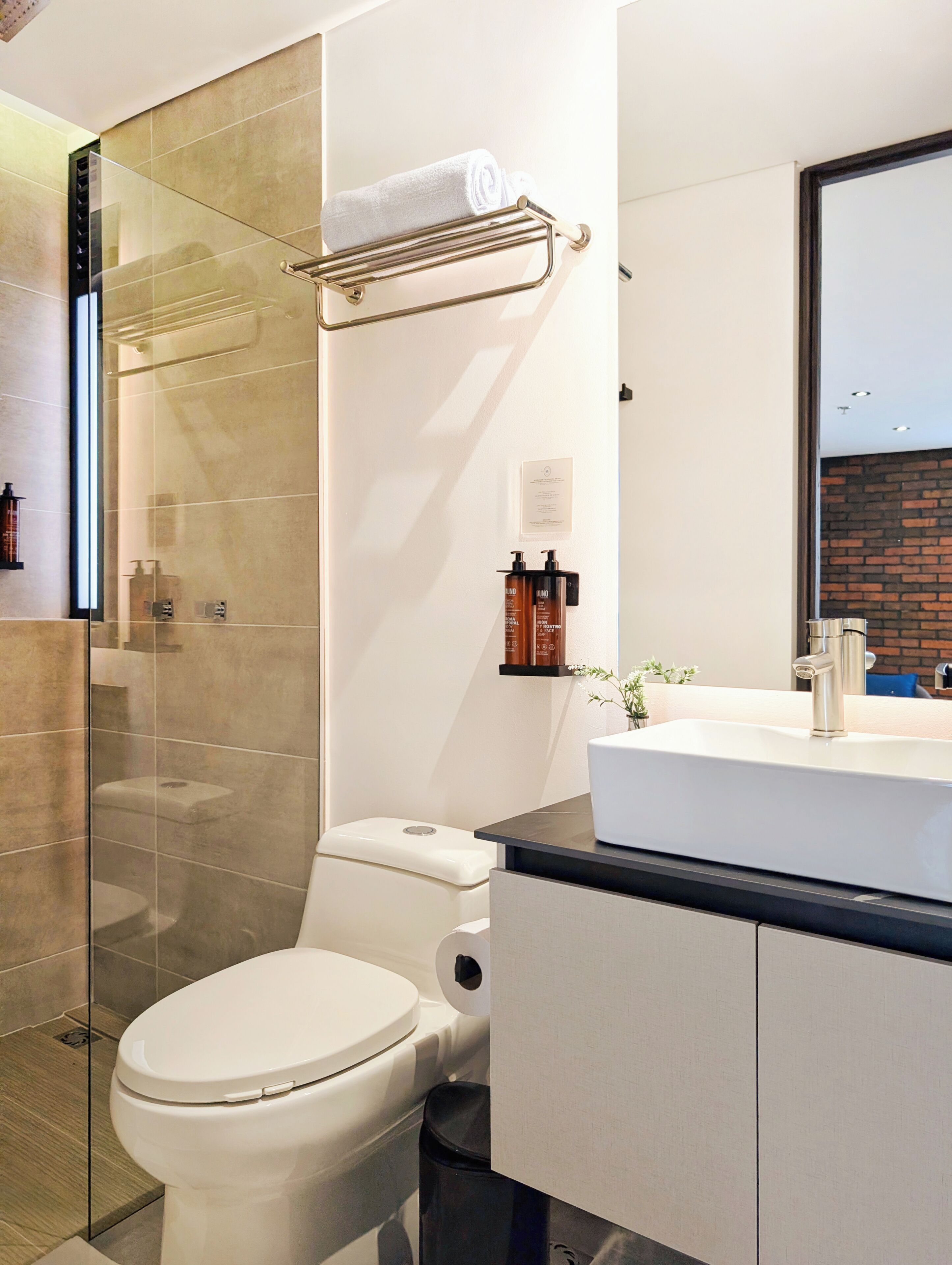 A modern bathroom with a glass shower enclosure, a white toilet, a sink with a black countertop, and a mirror above the sink.